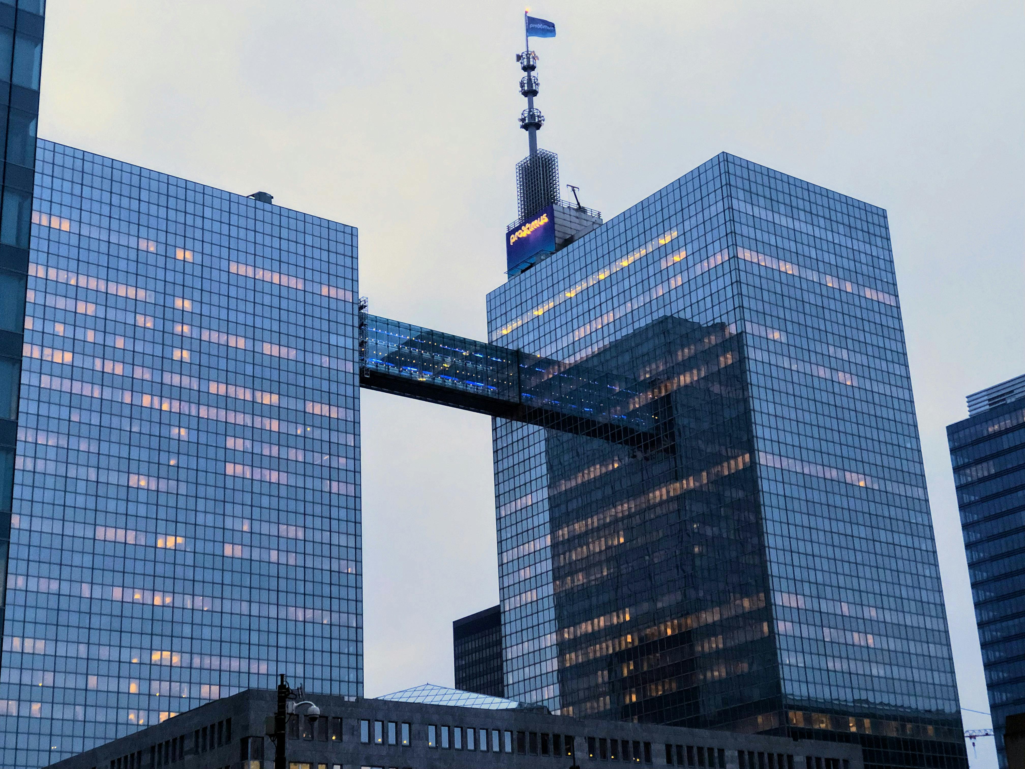 Texte pour Webex. Immeubles de bureaux modernes en verre avec un pont aérien reliant un ciel bleu avec des nuages roses.