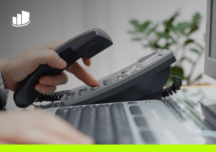 A close-up of a person dialing a desk phone while holding the handset.
