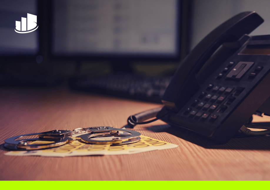 Handcuffs and cash beside office phone on desk, symbolizing telecom security risks.