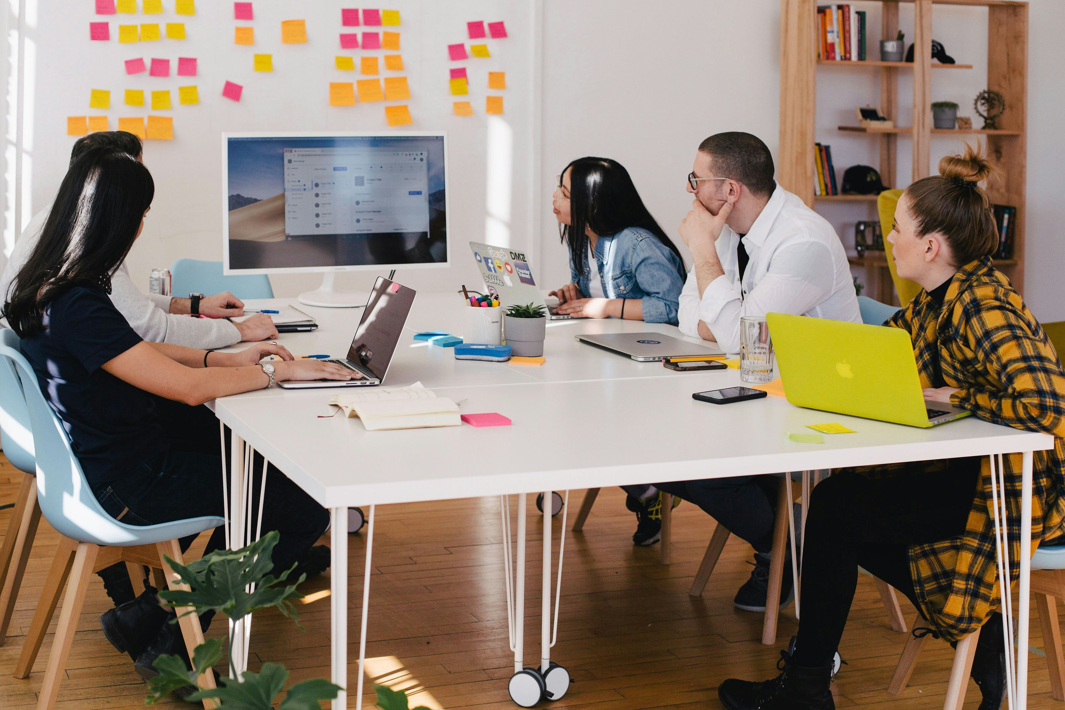 A diverse group of individuals collaborating around a table, each engaged with their laptops in a productive environment.