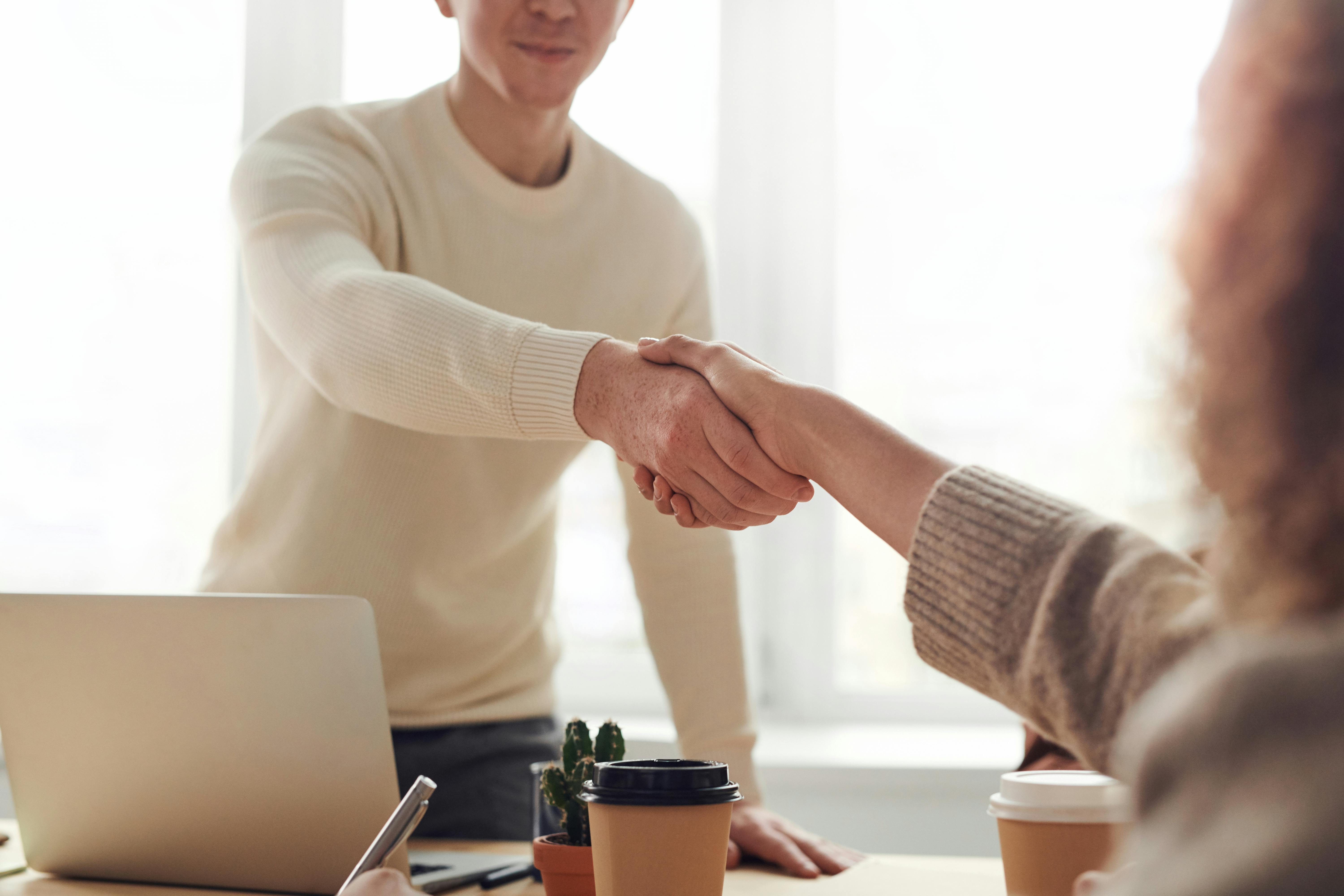 Operator Connect. A man and woman shaking hands over a desk, symbolizing agreement and collaboration in a professional setting.