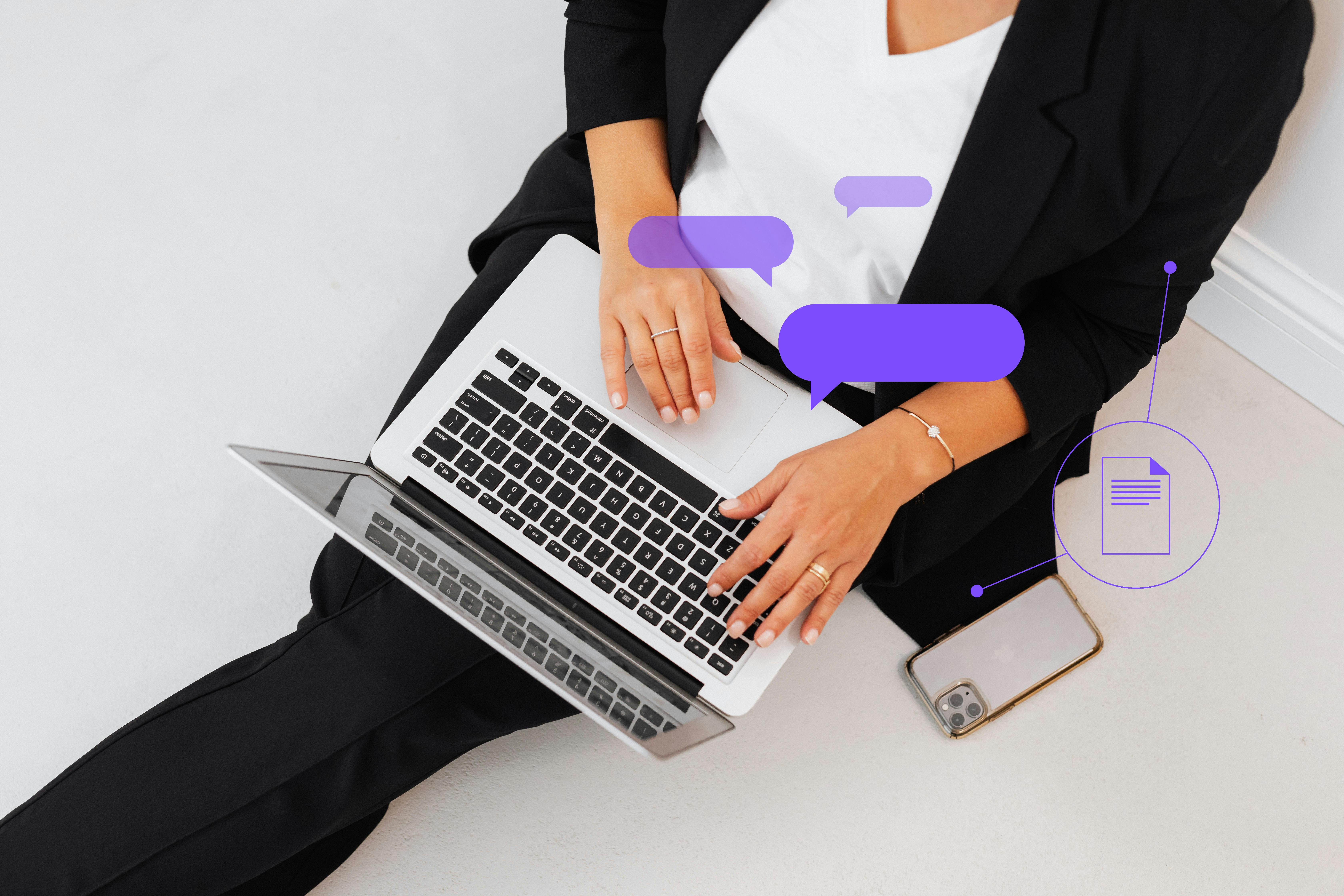 A woman dressed in a business suit is seated on the floor, working intently on her laptop, reflecting a modern work ethic.